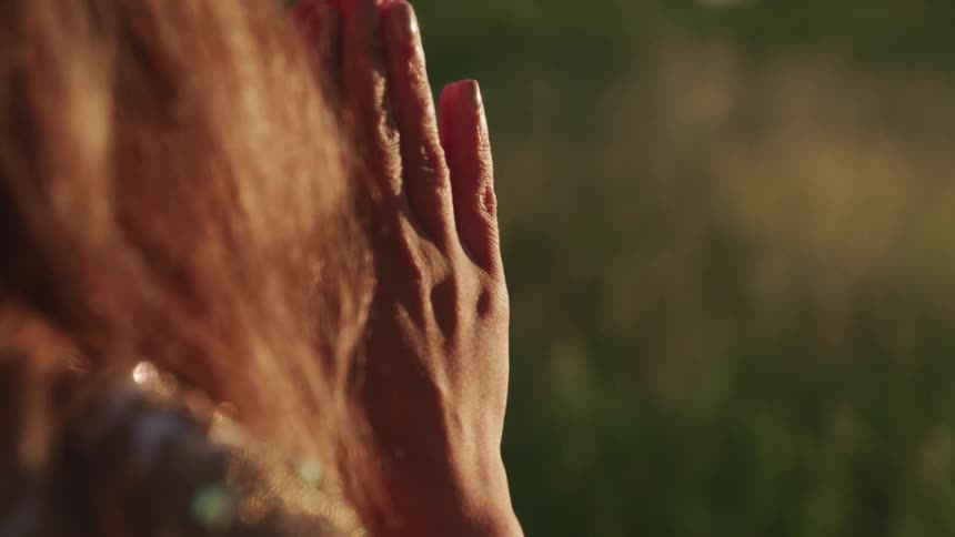 A person stands holding a hand up to obscured face
