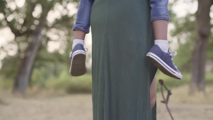 Child wearing tennis shoes on the back of their mother outdoors at daytime