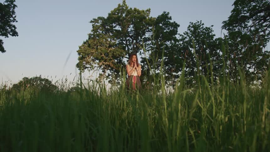 A woman stands in tall grass and prays