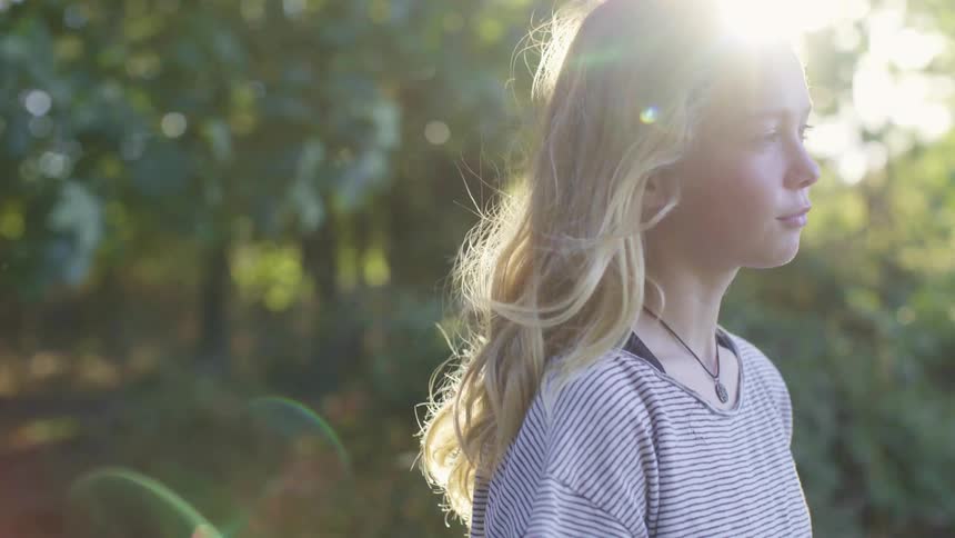 A young girl standing a forest closes her eyes
