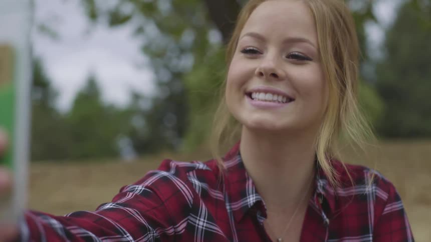 A woman takes a selfie with her cell phone while sitting outdoors in nature