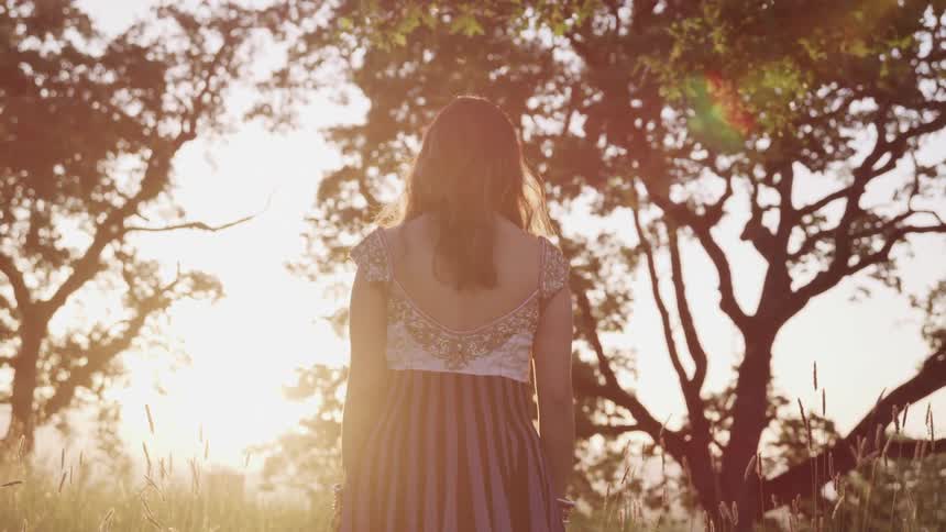 A woman in a sequin and striped dress walks toward trees in a field