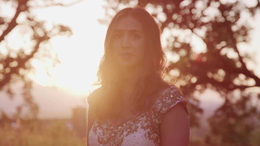 Woman stands outside looking at camera at sunset