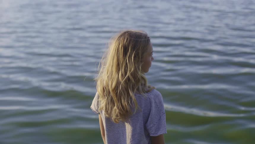 Girl with long hair and wearing a blouse watches water rolling in