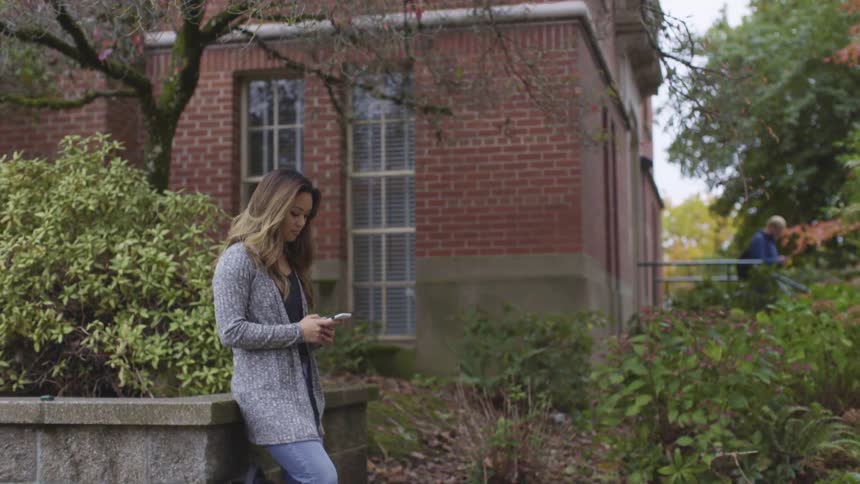 Woman stands leaning against large planter while a man walks out of a building behind her