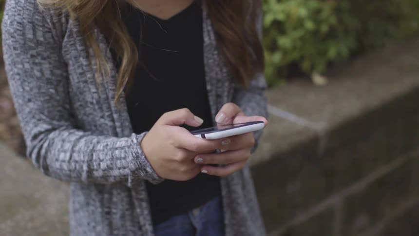 A woman stands outdoors texting on a phone during the day