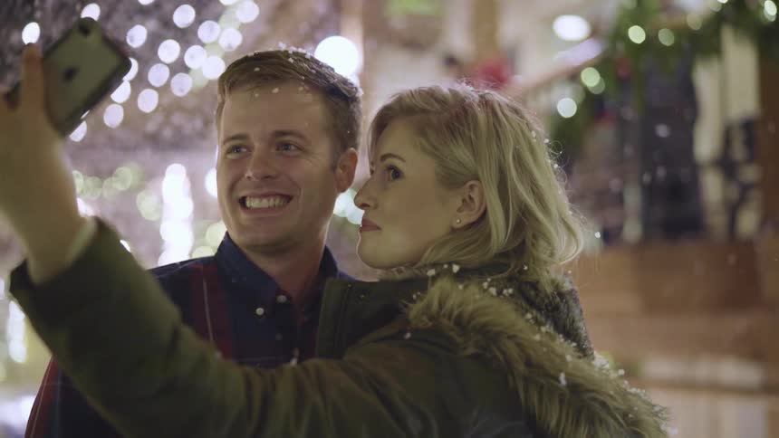 A woman with a smart phone taking a picture with a man in the snow