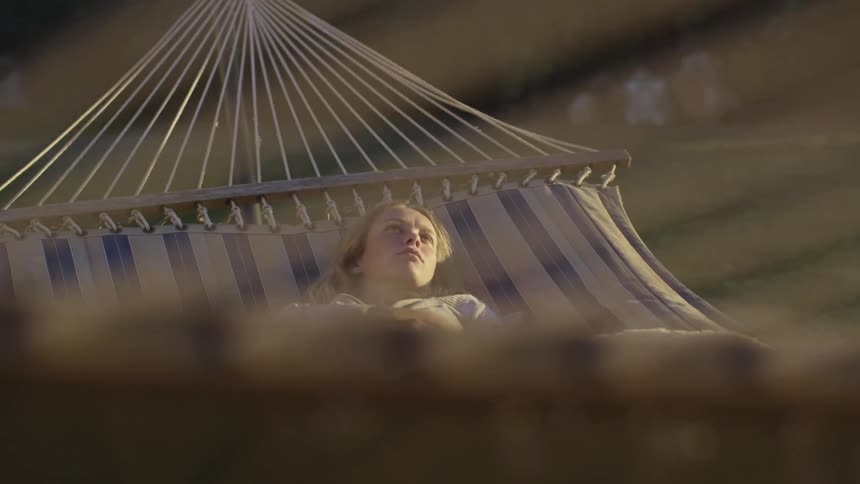 A young female reclines in the hammock outdoors while looking bored