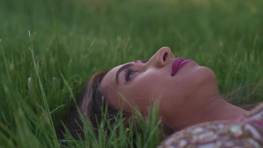 Woman lying down in the grass rests her eyes and stares up at the sky