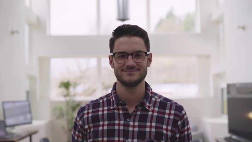 A young man takes a sip from a coffee mug before smiling into the camera while standing in a room in an expensive house