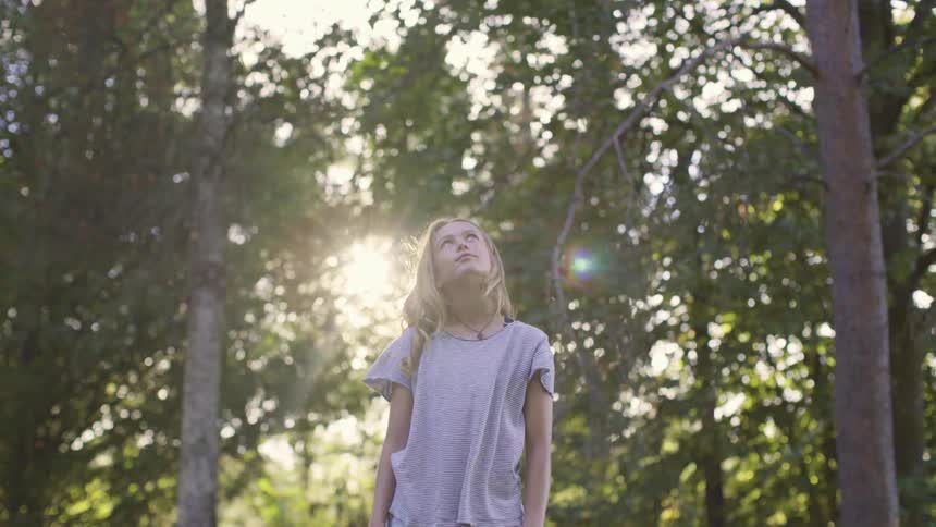 A pre teen girl wearing pajamas stands outside in a forest on a sunny day