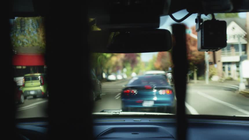 Vehicles travel along a road through a neighborhood during the day