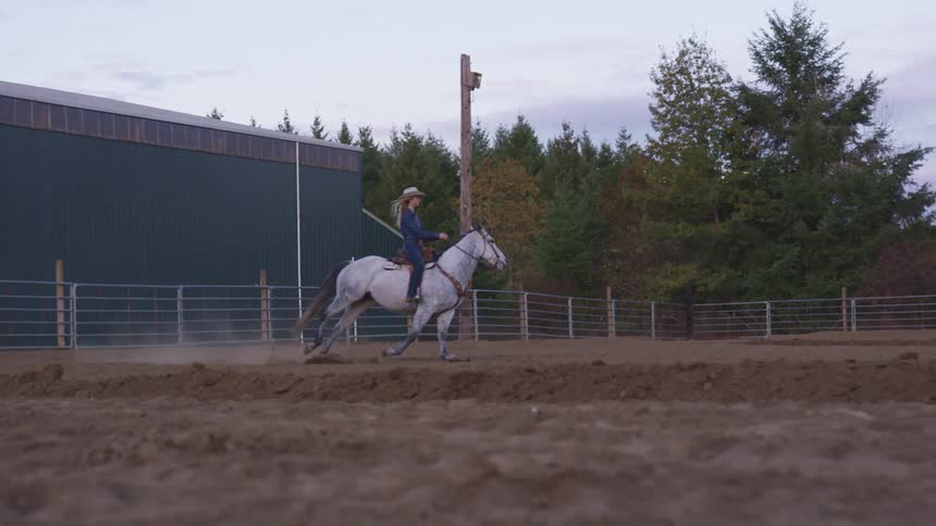 A woman rides a horse around a corral in the evening