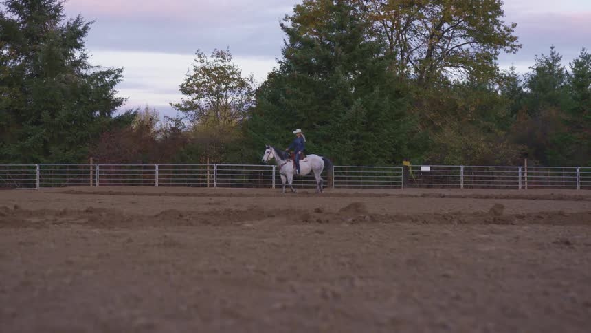 A woman is riding a horse outdoors at dusk