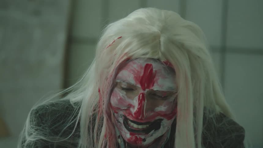 A woman laughs as she smears face paint on her face and neck