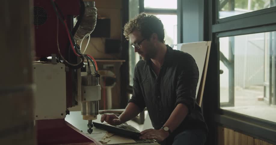 Man uses a computer near a machine inside a warehouse