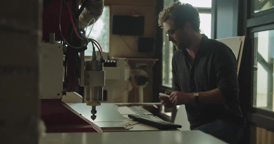 A man controls a wood carving machine and makes a small mark on the wood