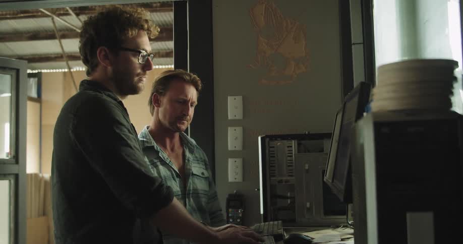 Two men working on a computer inside a warehouse at day time