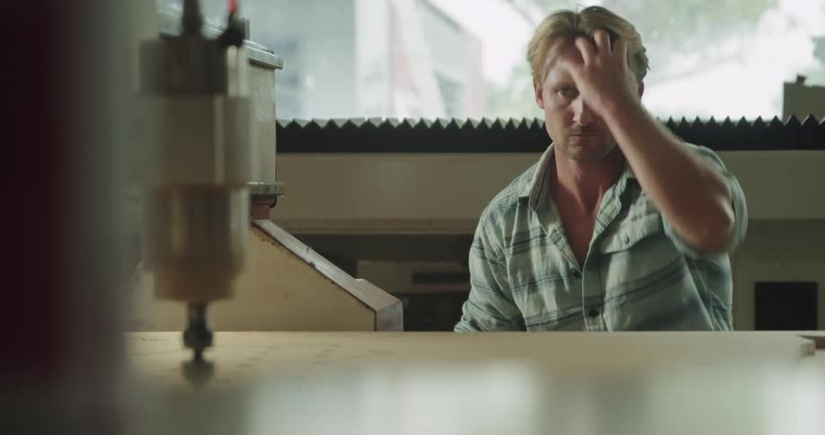 A blonde man sits and watches a machine while taking notes
