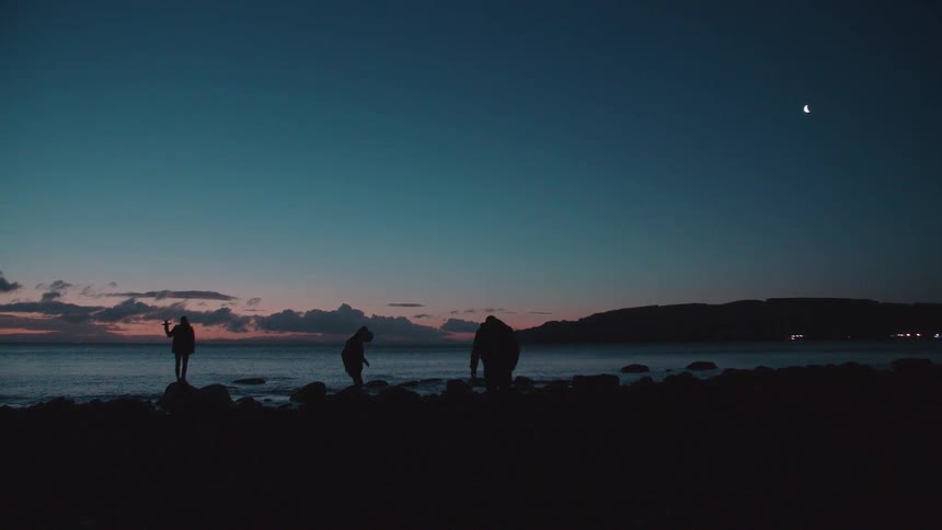 People walking on a rocky beach after sunset