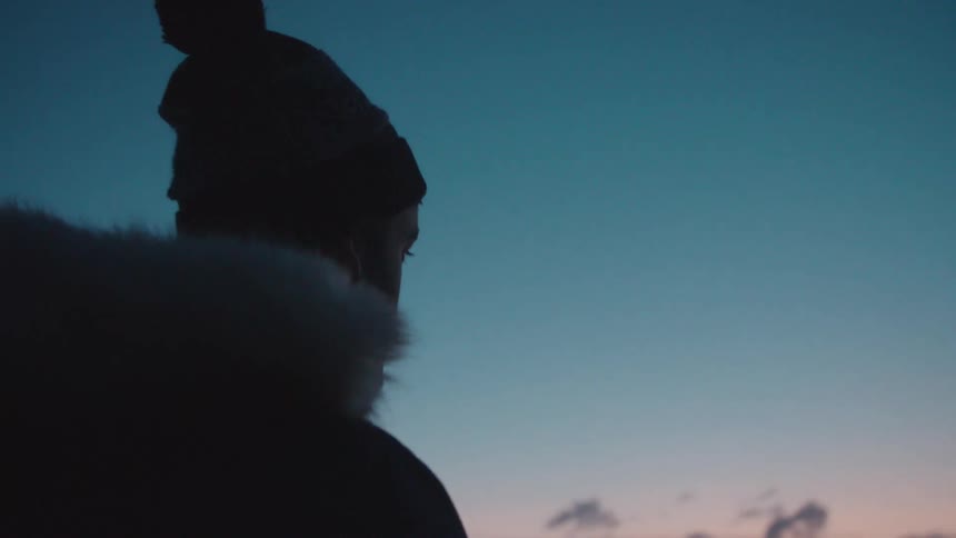 A man in a coat stares out at the sunset