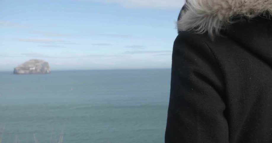 A person in a fur lined hood looks out at the water