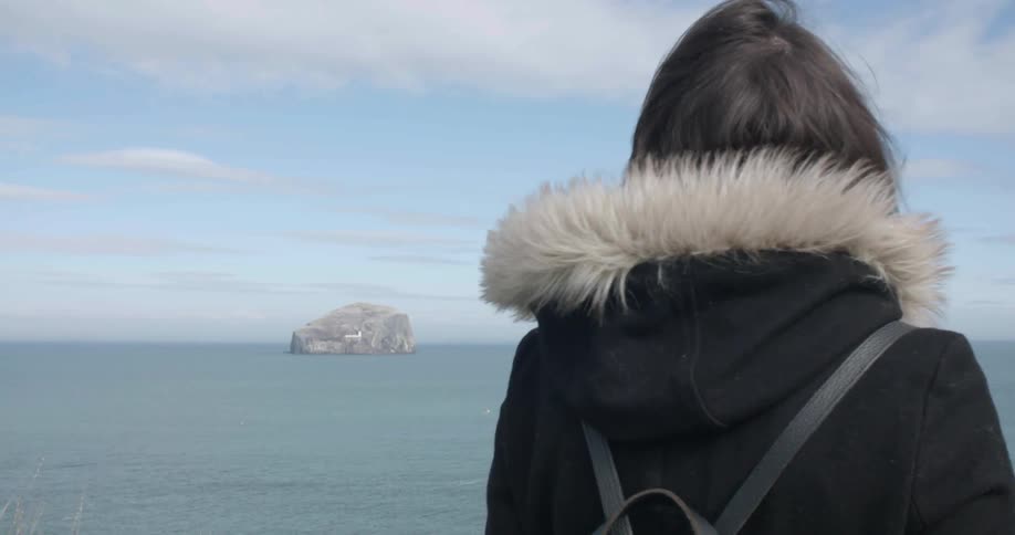 A woman is looking over towards the ocean on a cloudy day