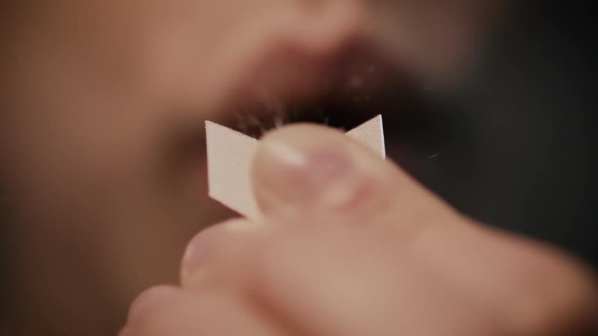Fingers holding a small piece of paper are blown on by lips