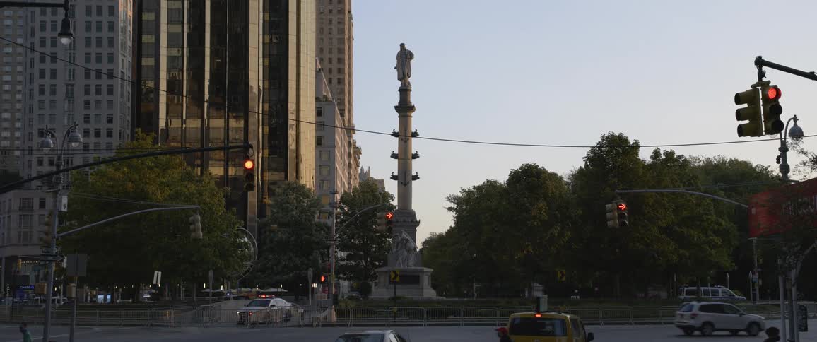 A tall monument looms over an intersection in a metropolis during the day