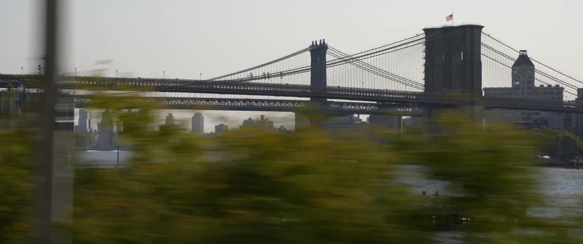 A bridge over water at sunset with an american flag on top and a city skyline in the background