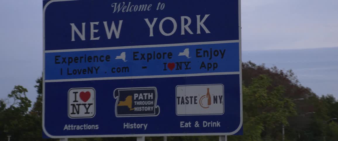 Cars driving by a welcome to new york sign on a summer day
