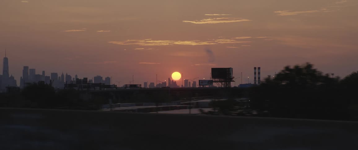 Red sky and huge setting sun with city buildings on the horizon and trees in the foreground