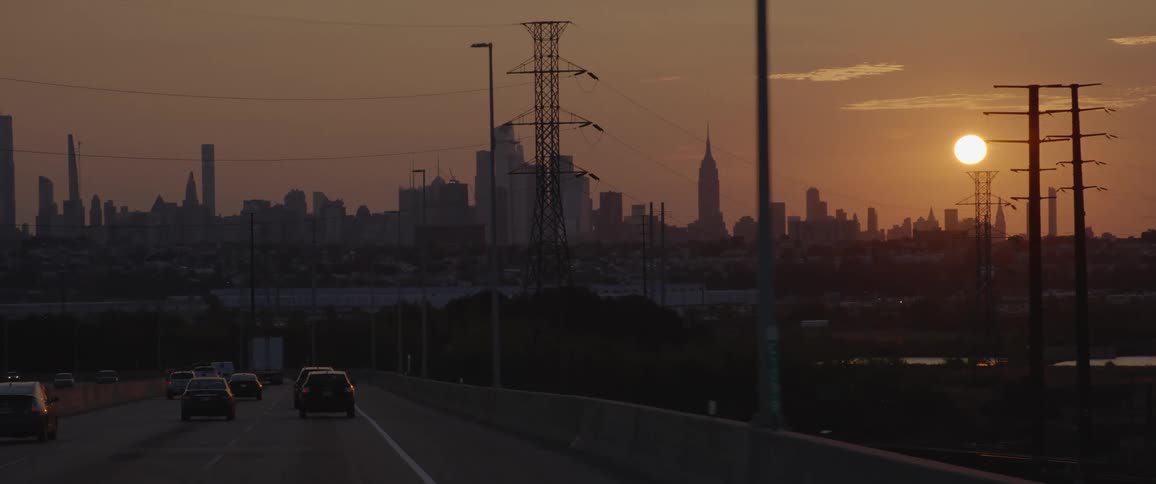 Sky shines over city turning foggy sky red as vehicles drive toward downtown skyline