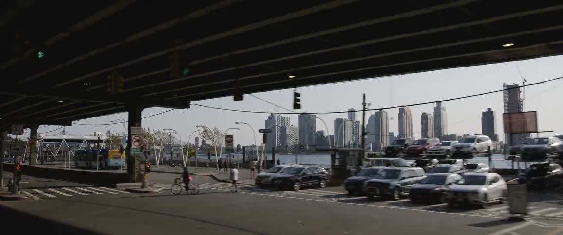 A city street on the shore with the skyline in the distance with vehicles driving people walking and riding bikes and a parking business