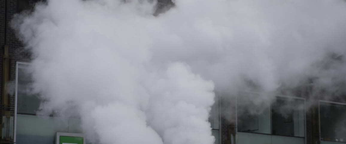 Steam pours out of two ducts and then a building is revealed afterwards