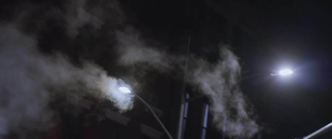 Twisting footage of clouds of steam coming out of a red chimney in new york city downtown street at night