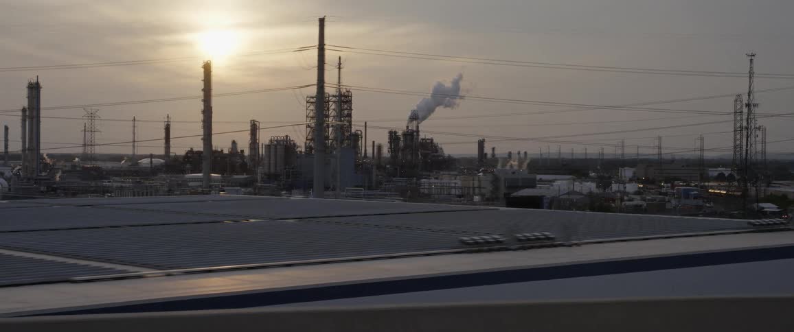Industrial complex in the horizon filmed from a moving car at sunset