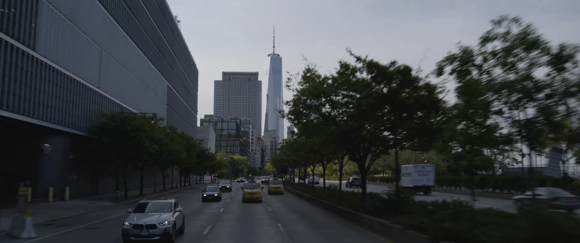 Traffic travels past large buildings and skyscrapers along a large road in a metropolis during the day