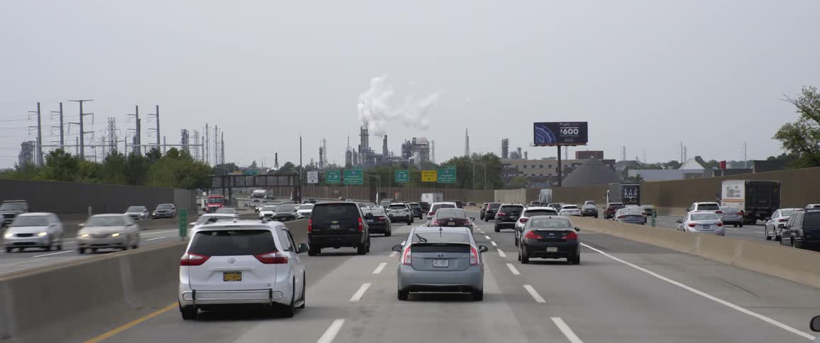 Vehicles driving down a highway towards the indusrial area at day time