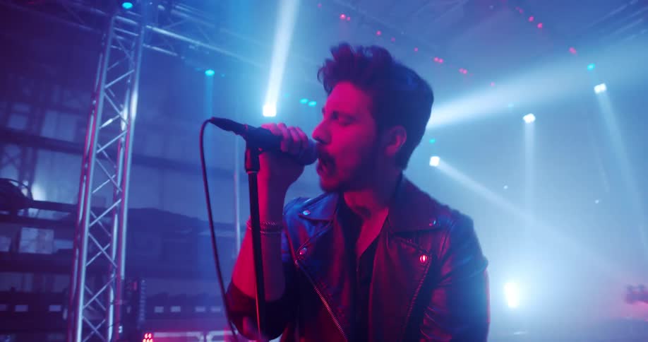 Musician sings during a concert while band members play instruments in the background