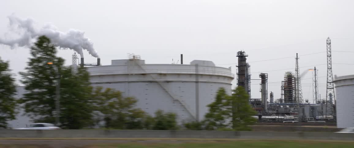 Traffic flows along highway passing refinery and tanks