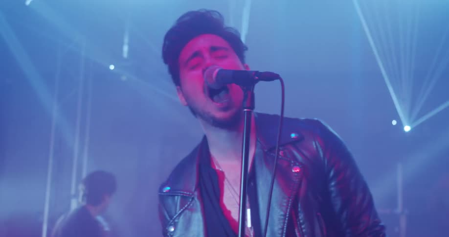 Bright lights flash as a man sings on stage and his band plays instruments
