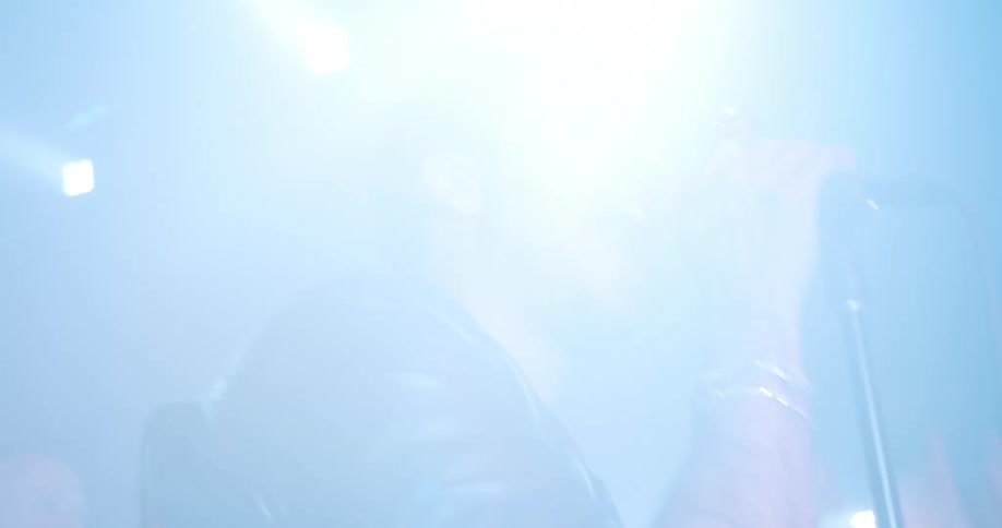 Man sings into microphone under strobing spot lights