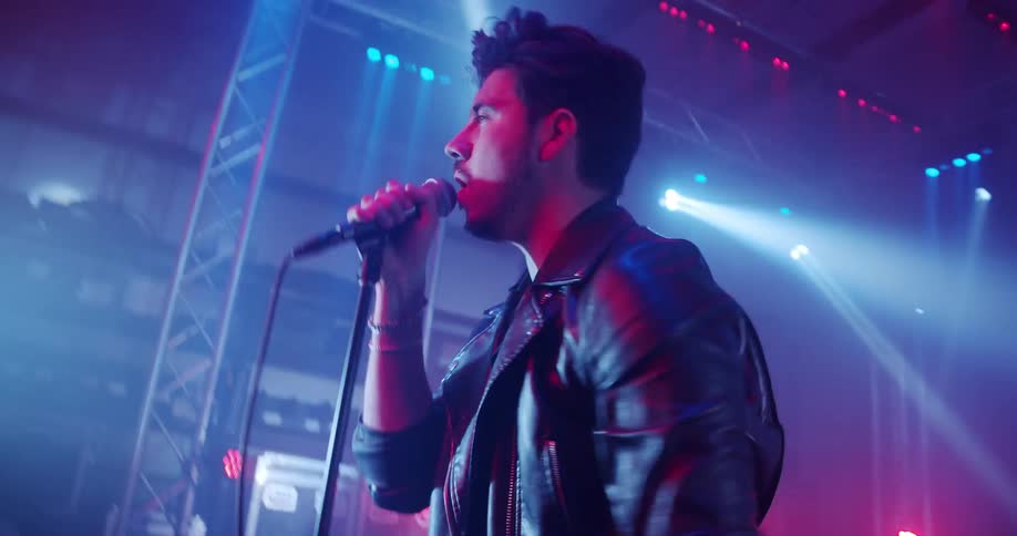 Bright lights flash as a man sings on stage and his band plays behind him