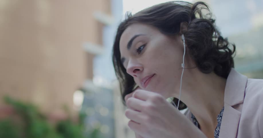 A woman dressed in business attire putting in earphones in downtown city area