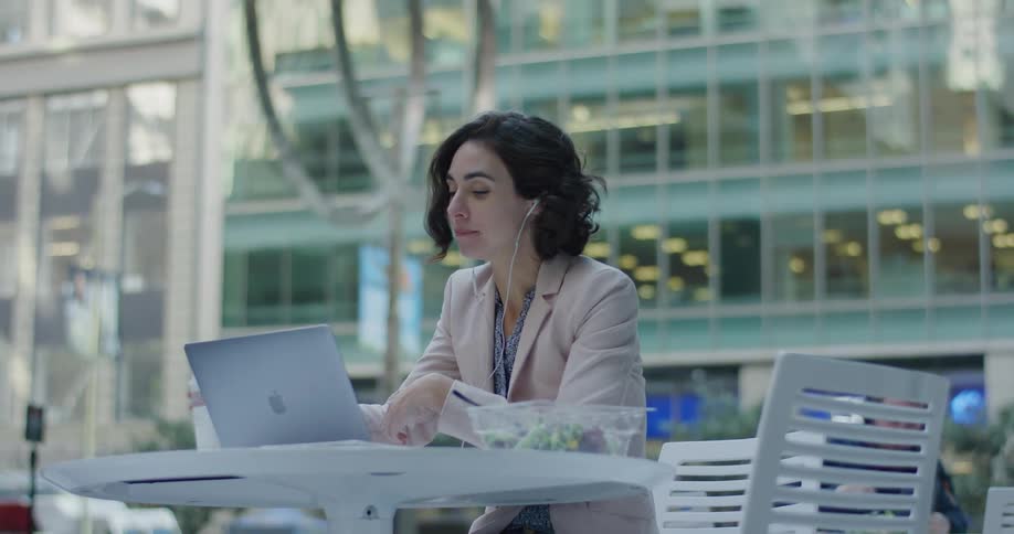 A woman drinks coffee while using her laptop outside