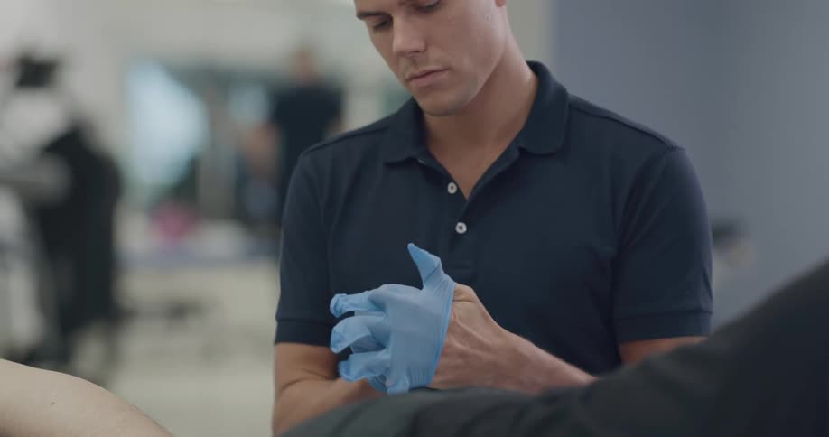 A man is putting on blue gloves in front of a person lying prone in front of him