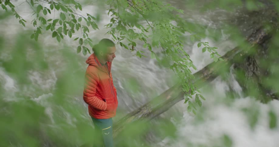 Man standing next to a down tree across a fast flowing river