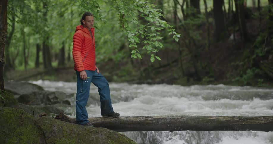 A man is balancing on a log over the stream