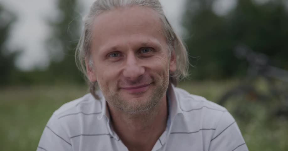 Man with grey hair faces the camera with eye contact in the field
